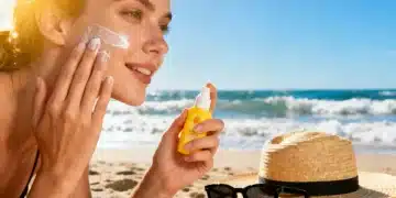 Woman applying sunscreen on beach in summer 2026, protecting skin from UV rays.